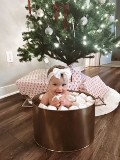 a baby sitting in a tub next to a christmas tree