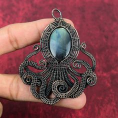 a hand holding an ornate pendant with a blue stone in the center and black filigrees around it