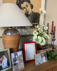 a table topped with pictures and a lamp next to a vase filled with flowers on top of a wooden table