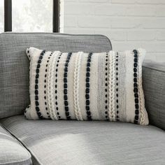 a gray couch with a black and white striped pillow on it's back, in front of a brick wall