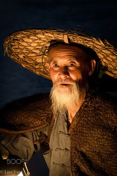 an old man with a long white beard wearing a straw hat and looking at the camera