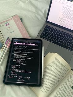 an open laptop computer sitting on top of a bed next to notebooks and pens