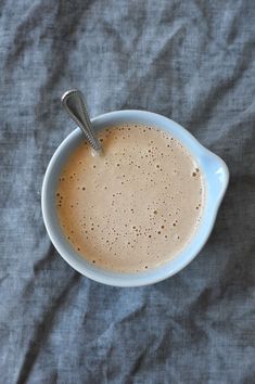 a cup of coffee with a spoon in it sitting on a gray cloth covered tablecloth