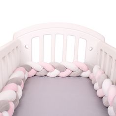 a white crib with pink, grey and white pillows on the bottom half of it