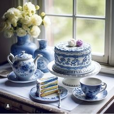 there is a blue and white cake on the table next to two teacups