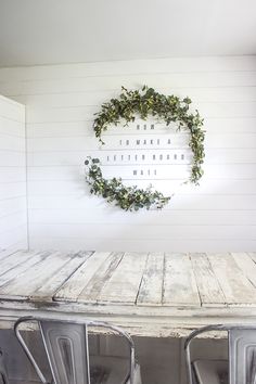 a table and chairs in front of a white wall with a wreath on the wall