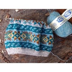 a blue and white knitted mitt next to a ball of yarn on the ground