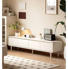 a living room scene with focus on the sideboard and plant in the foreground