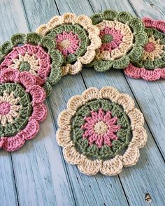 several crocheted coasters are arranged on a wooden surface, one is green and the other is pink