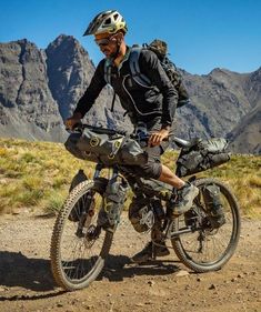 a man riding a bike on top of a dirt field next to mountains in the background