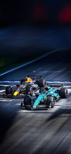 three race cars racing on a track in the dark, one is blue and yellow