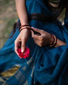 a woman sitting on the ground holding onto a flower with both hands and wearing bracelets