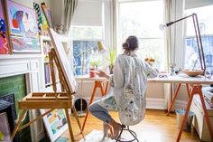 a woman sitting at a desk in front of an easel with paintings on it