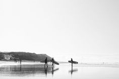 black and white photograph of people carrying surfboards on the beach