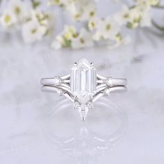 an emerald cut diamond engagement ring on a white background with flowers in the foreground