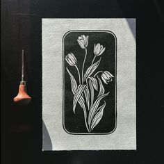 a black and white drawing of flowers on a piece of paper next to a needle