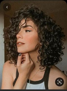 an image of a woman with curly hair looking up and to the side while holding her hand on her chin