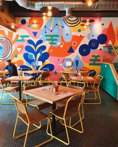 the interior of a restaurant with brightly painted murals on the wall and wooden tables in front of them