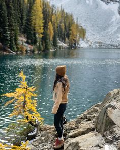 a woman standing on top of a rock next to a lake