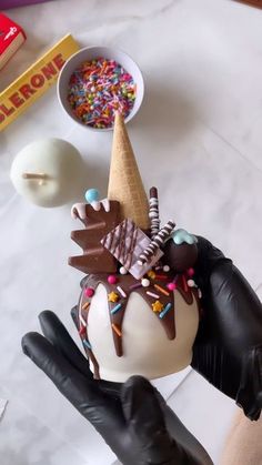 an ice cream sundae with chocolate and sprinkles on top is being held by a gloved hand