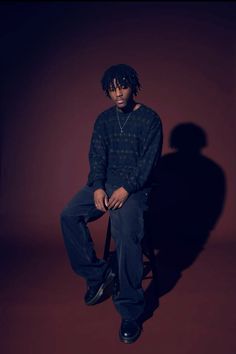 a man with dreadlocks sitting on a stool in front of a red wall