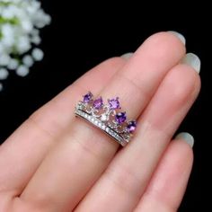 a woman's hand holding a purple and white ring with three diamonds on it