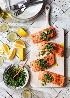 three salmon fillets on a cutting board with lemons and parsley next to it