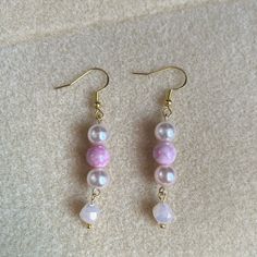 two pink and white beads are hanging from gold earwires on a beige carpet