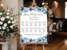 a blue and white floral wedding seating plan on an easel with flowers in the background