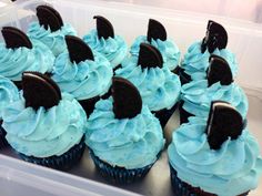 cupcakes with blue frosting and oreo cookies on top in a plastic container