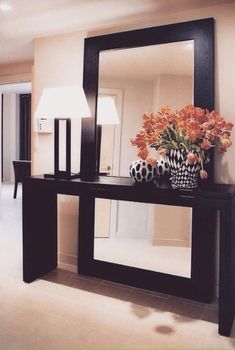 a large mirror sitting on top of a table next to a vase filled with flowers