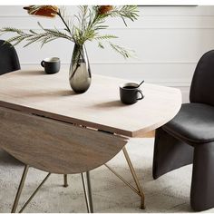 a wooden table with two black chairs and a vase on the table next to it