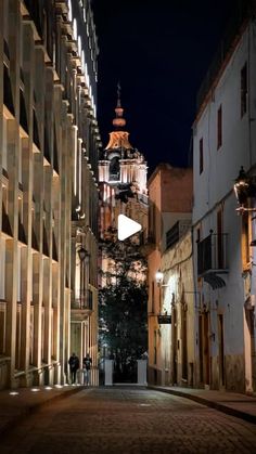 an empty street at night with tall buildings on both sides and a clock tower in the distance