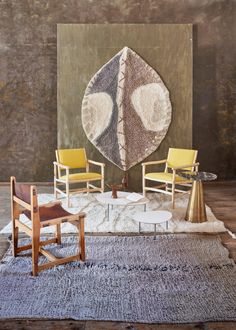 two chairs and a table in front of a large rug with an abstract design on it