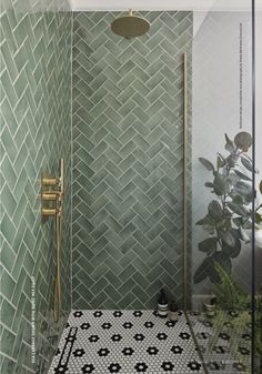 a green tiled shower with black and white tiles on the floor, along with a gold faucet