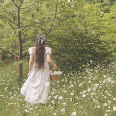 a woman in a white dress walking through a field with daisies