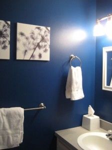 a bathroom with blue walls and white towels hanging on the wall, along with two framed pictures