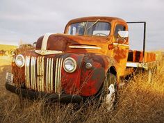 an old rusted truck sitting in the middle of a field