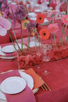 the table is set with pink and orange flowers in vases, watermelon napkins, and silverware