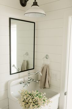 a white sink sitting under a mirror next to a bath tub with flowers in it