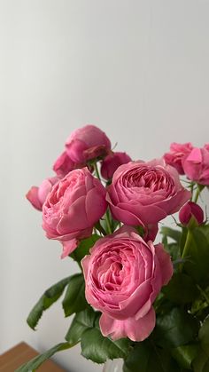 a vase filled with pink roses sitting on top of a wooden table next to a white wall