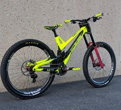 a yellow and black mountain bike parked next to a gray wall with graffiti on it