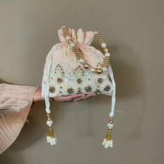 This Pearl and Zirconia and Sequin studded Peach Potli is a beautifully handcrafted Indian Batwa Bag, perfect for adding a touch of traditional elegance to any occasion. The bag features a stunning peach base adorned with intricate pearl embroidery, creating a luxurious and festive appeal. The shimmering sequins add a glamorous flair, making it an ideal accessory for brides or wedding guests. ✅ How To Order Please select your color in option. ✅ SPECIFICATIONS: ⦿  Available in 3 colors : Hot pink, Baby blue, Peach  ⦿ Dimension: Length 9", Width 9" ⦿ Item Type: Indian Potli Bag ⦿ Material: Fabric, Sequins, Zardosi, Etc. ⦿ Gender: Women ✅ FEATURES: ⦿ Made using beads and sequins and rhinestones on silk fabric ⦿ Ethnic and contemporary ⦿ Has a drawstring closure ⦿ Add a touch of glamour ⦿ Plea Festive Pink Embellished Bag, Festive Pink Embellished Bags, White Clutch For Wedding And Festivals, Elegant Pink Pouch For Wedding, Elegant Pink Wedding Pouch, Pink Festive Potli Bag For Reception, Elegant White Bag With Zari Work, Wedding Festivals Handheld Potli Bag, Wedding And Festival Handheld Potli Bag