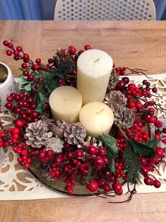 a table topped with candles and evergreens on top of a wooden table next to a cup