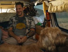 a man sitting in the back of a van with two dogs looking at him and smiling