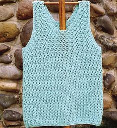 a knitted tank top hanging on a clothes rack in front of a stone wall