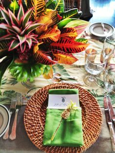 a place setting with green napkins, silverware and colorful flowers in the background