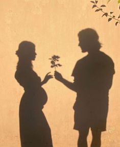 two people standing next to each other near a wall with a shadow on the wall