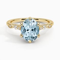 an oval aqua blue topaz ring with diamonds on the band and side stones in yellow gold