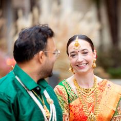 a man standing next to a woman in a green shirt and yellow sari smiling at each other